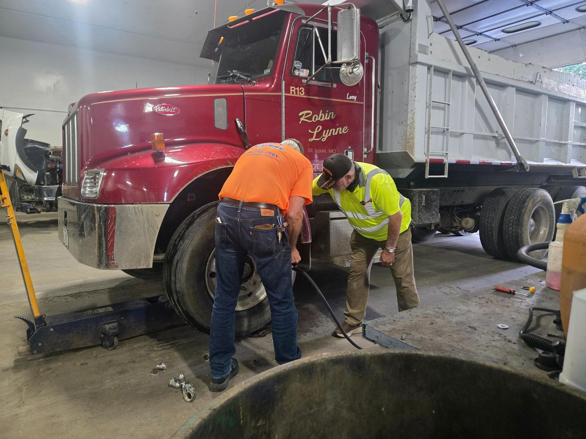 Workers repairing a red dump truck in an industrial garage, using tools near an open pit