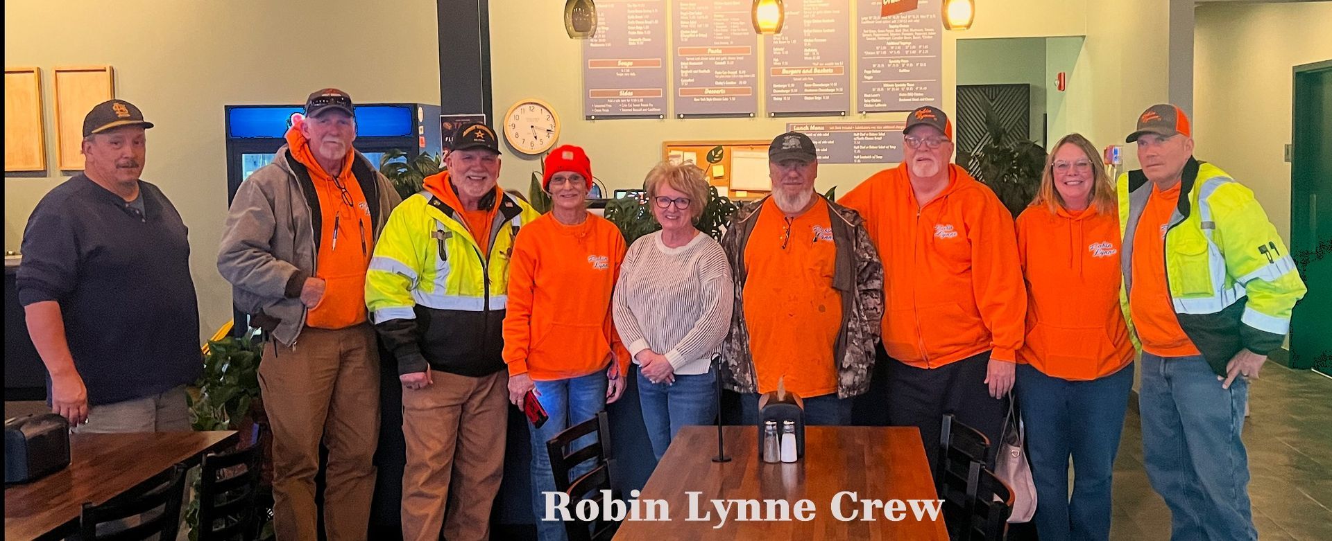The Robin Lynne crew standing together in a restaurant, many wearing bright orange shirts and caps.