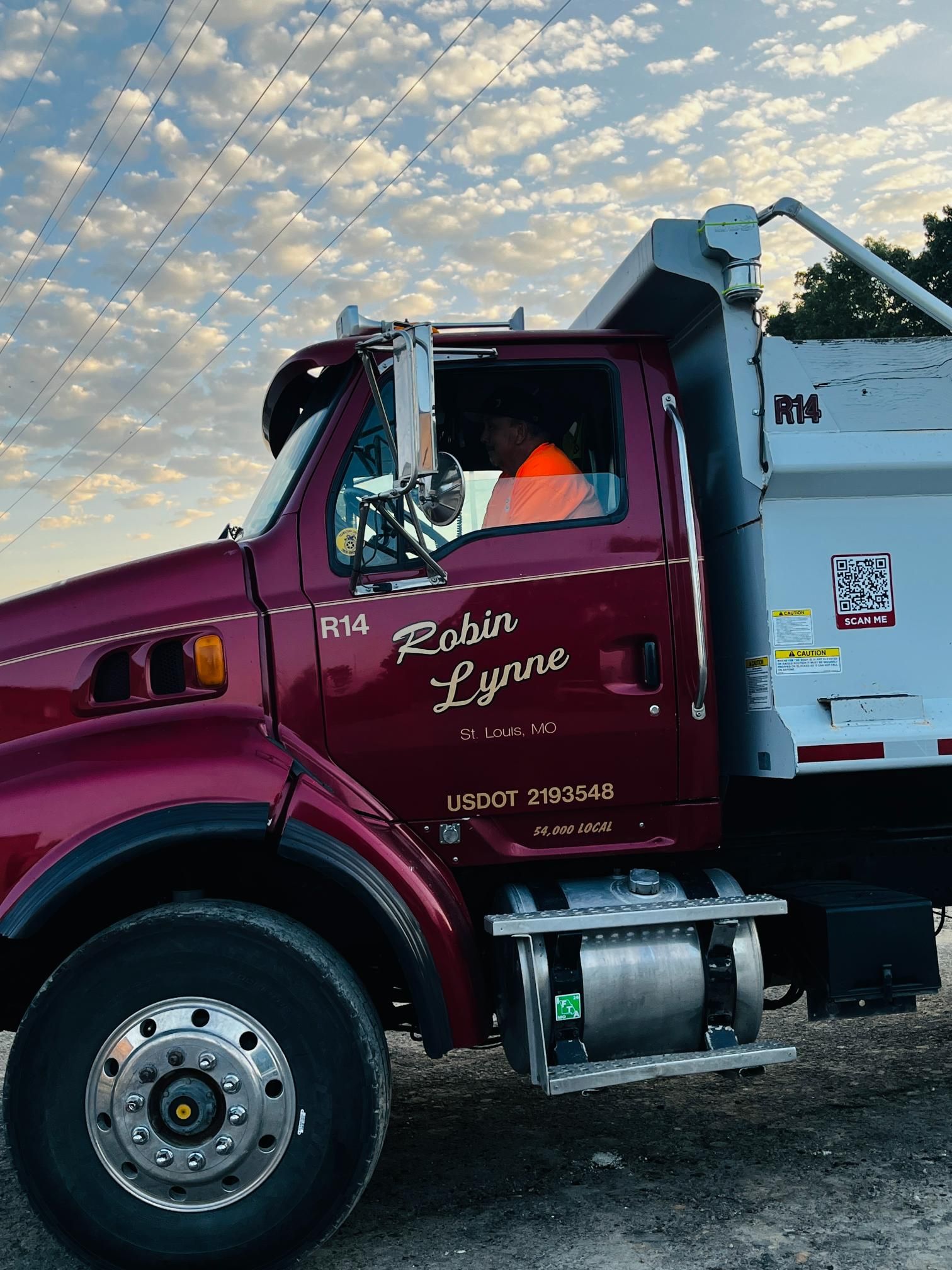 Maroon semi truck with white trailer parked on gravel under a cloudy sky
