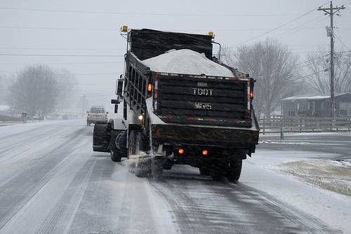 A snowplow truck spreading salt on a snowy road.