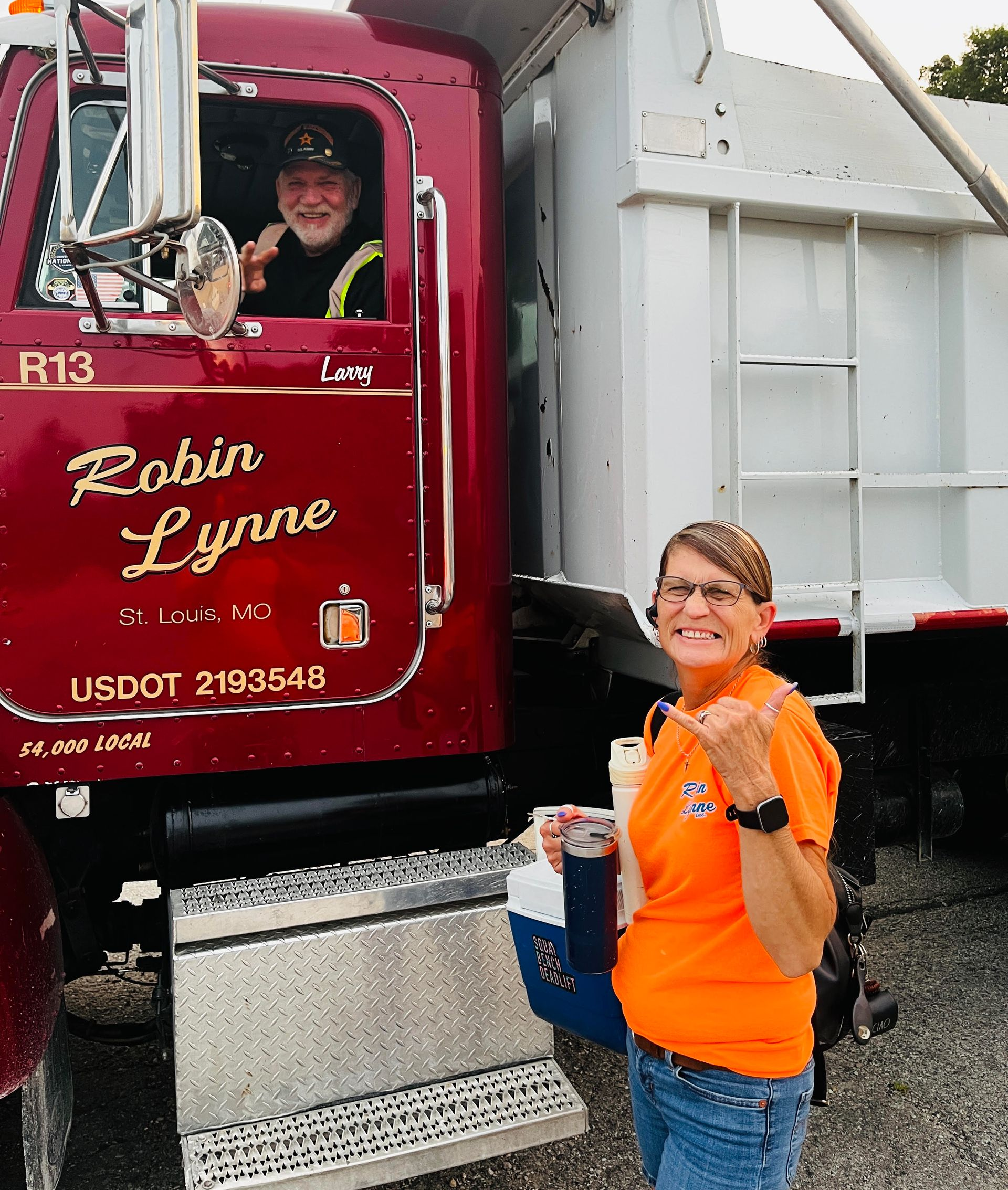 Person in orange shirt standing by a red Robin Lynn truck, with a driver visible inside.