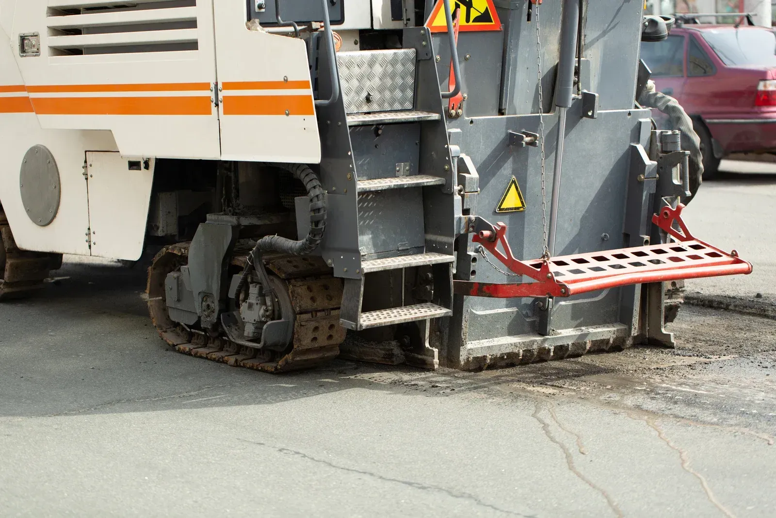 Asphalt milling machine removing pavement on a city street; orange, white, and gray.