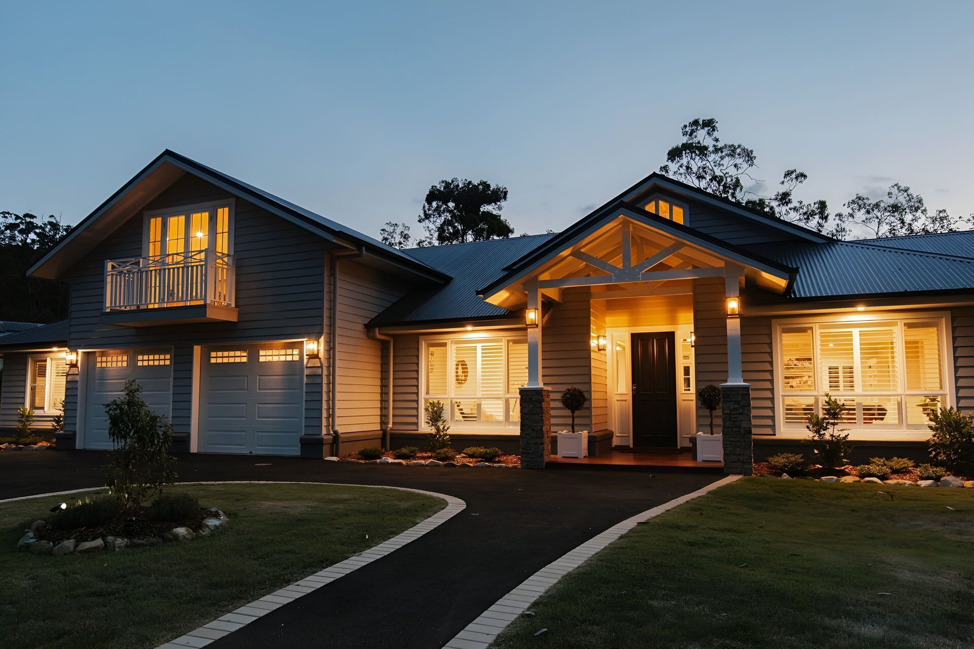 A modern house with a glowing interior, illuminated garage, and balcony, set against a twilight sky. — Michael Duncan Constructions Pty Ltd in Mermaid Beach, QLD