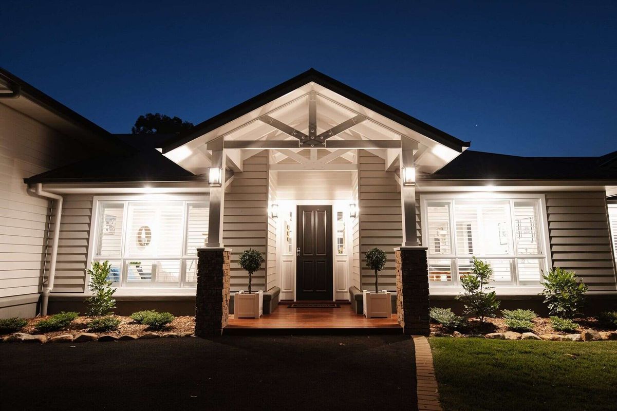 A modern house with a gabled entrance, dark door, and warm outdoor lighting at night — Michael Duncan Constructions Pty Ltd in Robina, QLD