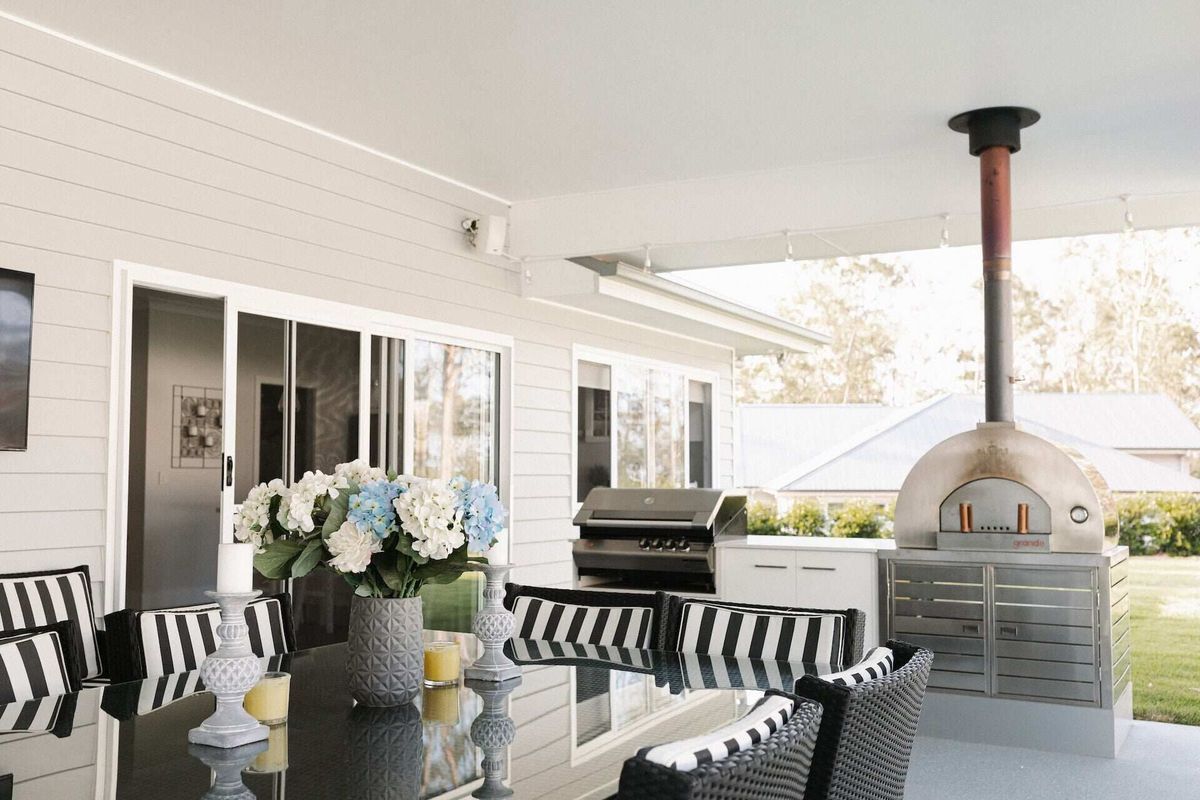A patio with a dining table, a flower centerpiece, a grill, and an outdoor pizza oven under a covered roof — Michael Duncan Constructions Pty Ltd in Robina, QLD