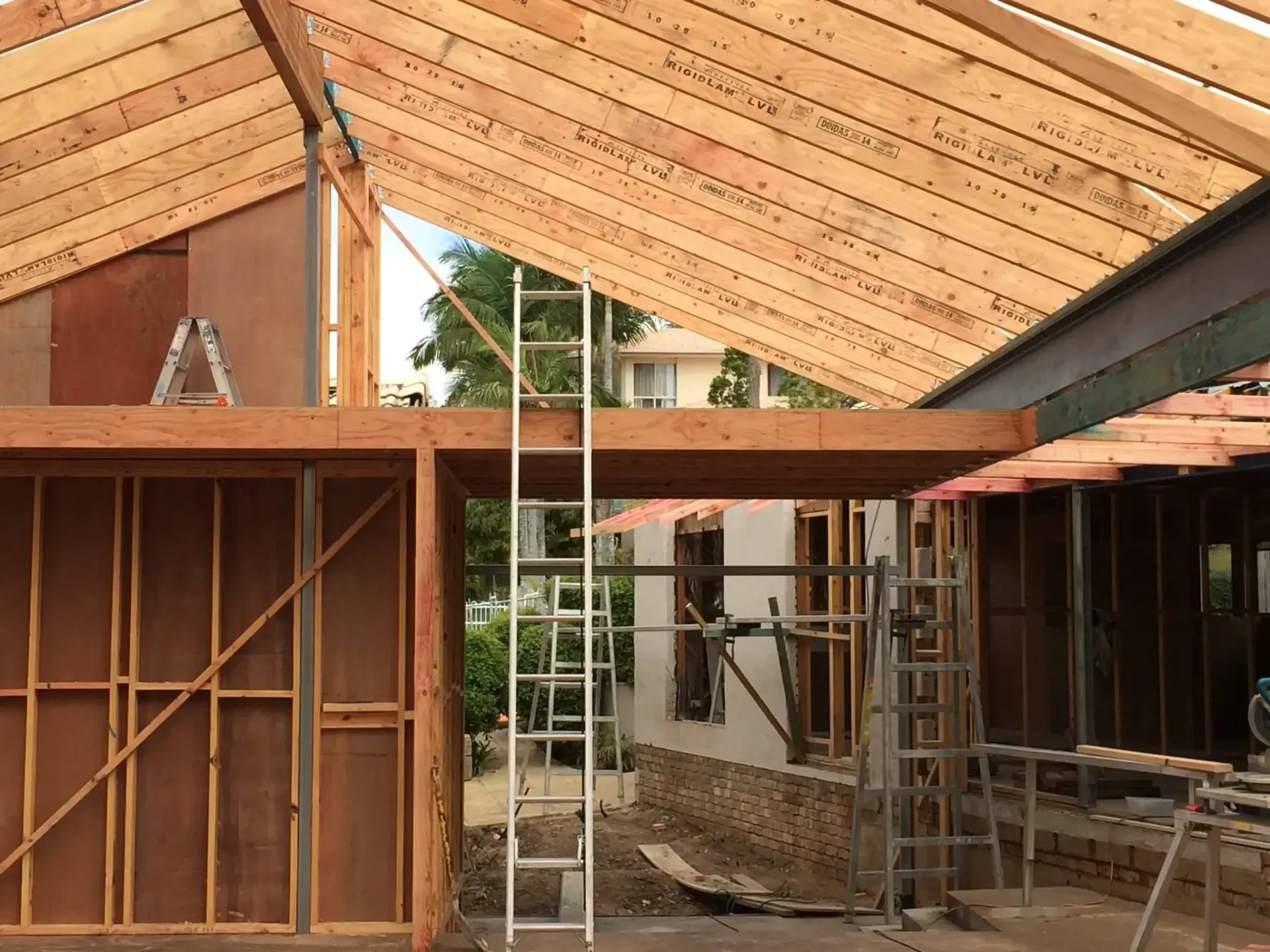 Construction site showing unfinished wood framing, a metal support beam, scaffolding, and ladders under a gabled roof. — Michael Duncan Constructions Pty Ltd in Robina, QLD