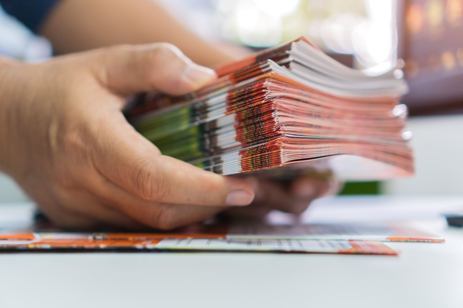 A person is holding a stack of magazines in their hands.