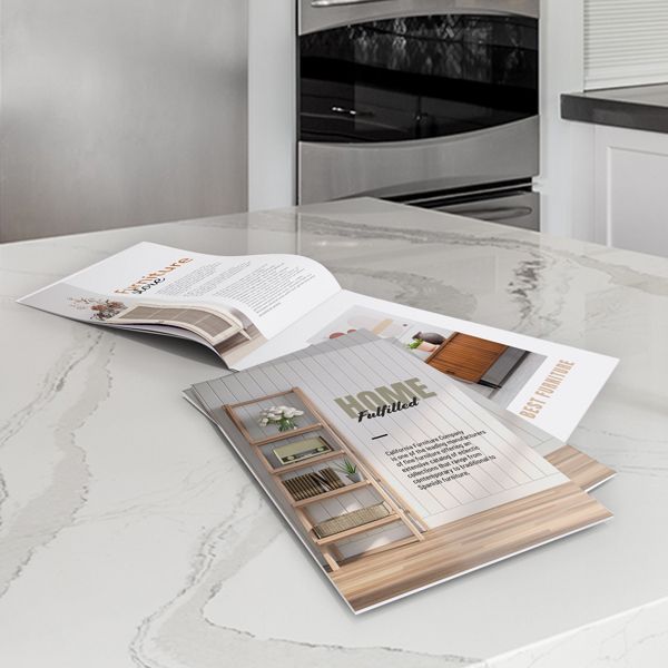 Brochure about home furniture on a marble countertop, with a blurred oven and kitchen cabinet in the background.