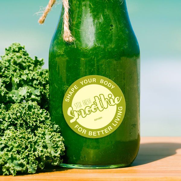 Green smoothie bottle with a label, next to kale leaves on a wooden surface.