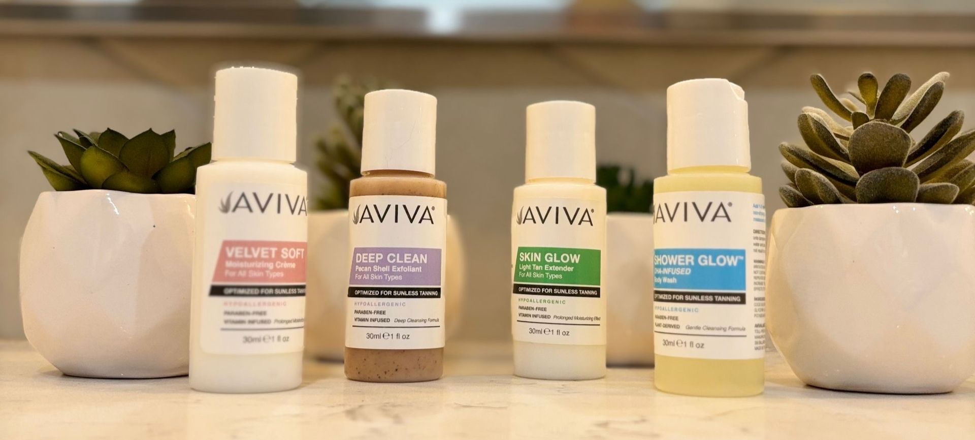 Four AVIVA skincare bottles in pastel labels lined up on a wooden surface