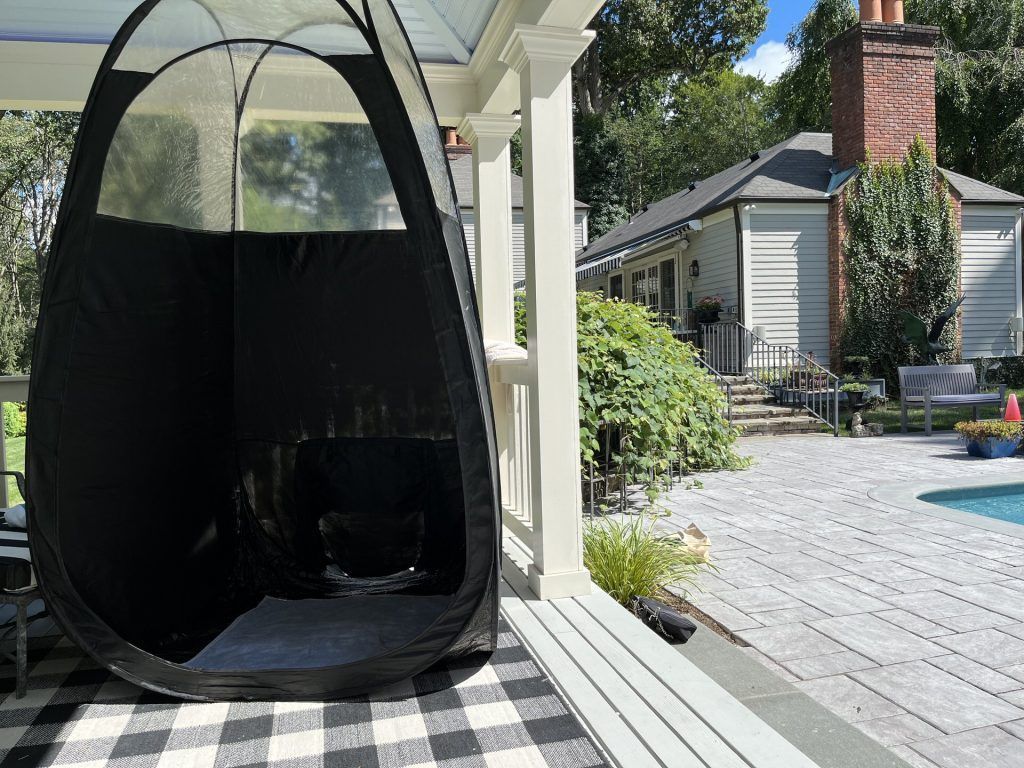 Black outdoor hanging pod chair on a covered patio beside a pool and brick house.