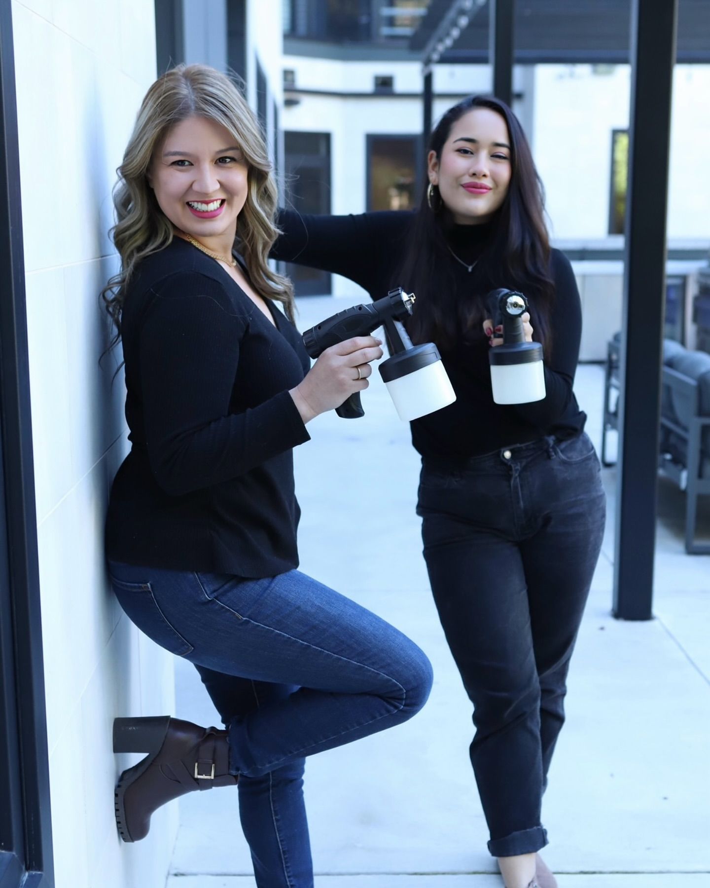 Two people posing with white bottles in a bright hallway, both dressed in black.