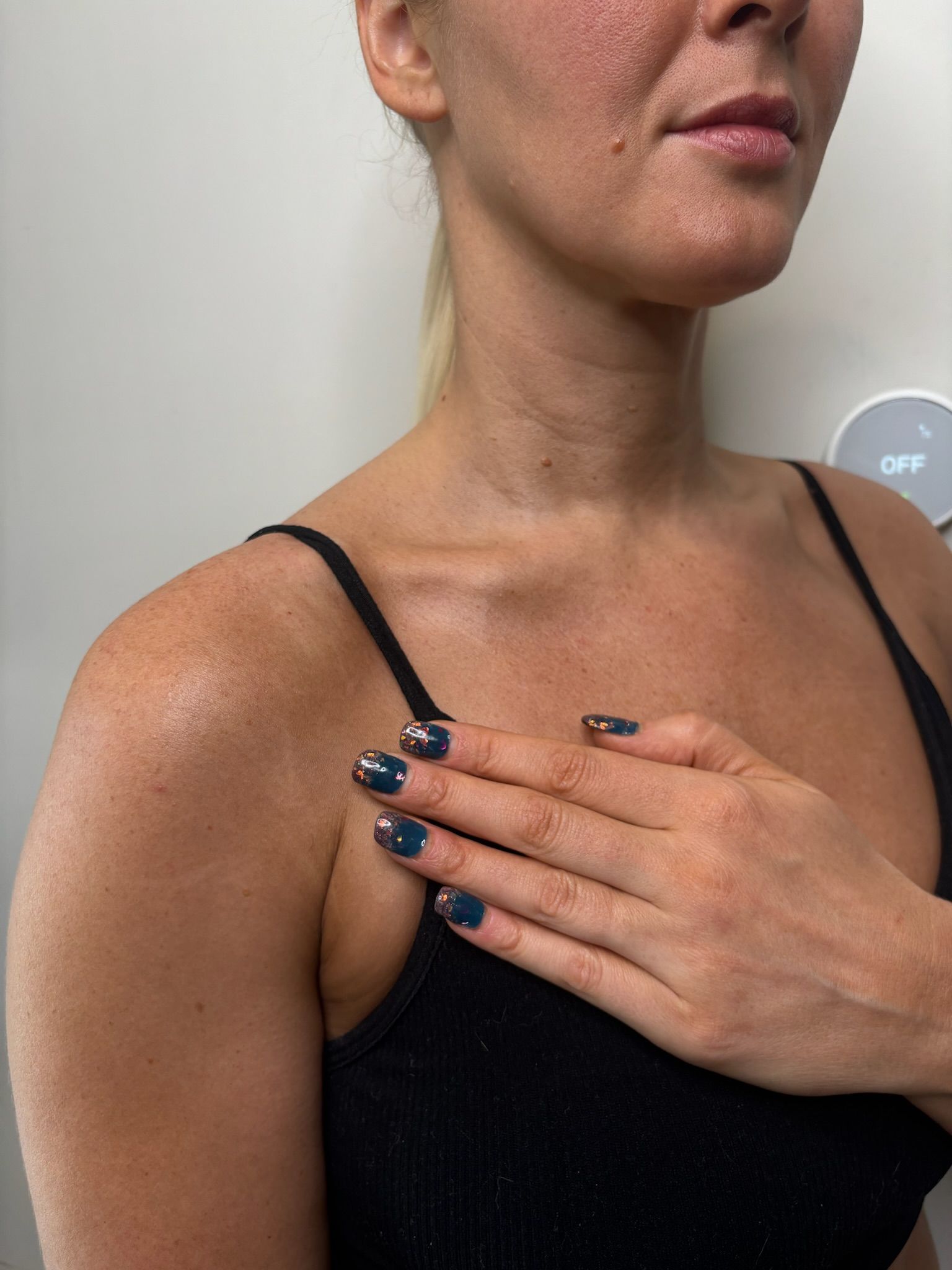 Woman in a black tank top touching her upper chest and neck with a black nail polish manicure