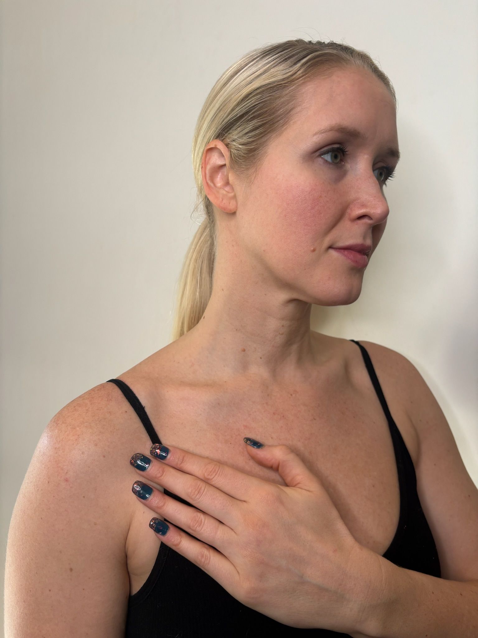 Woman in black spaghetti-strap top, side profile, hand on chest, against a plain background.