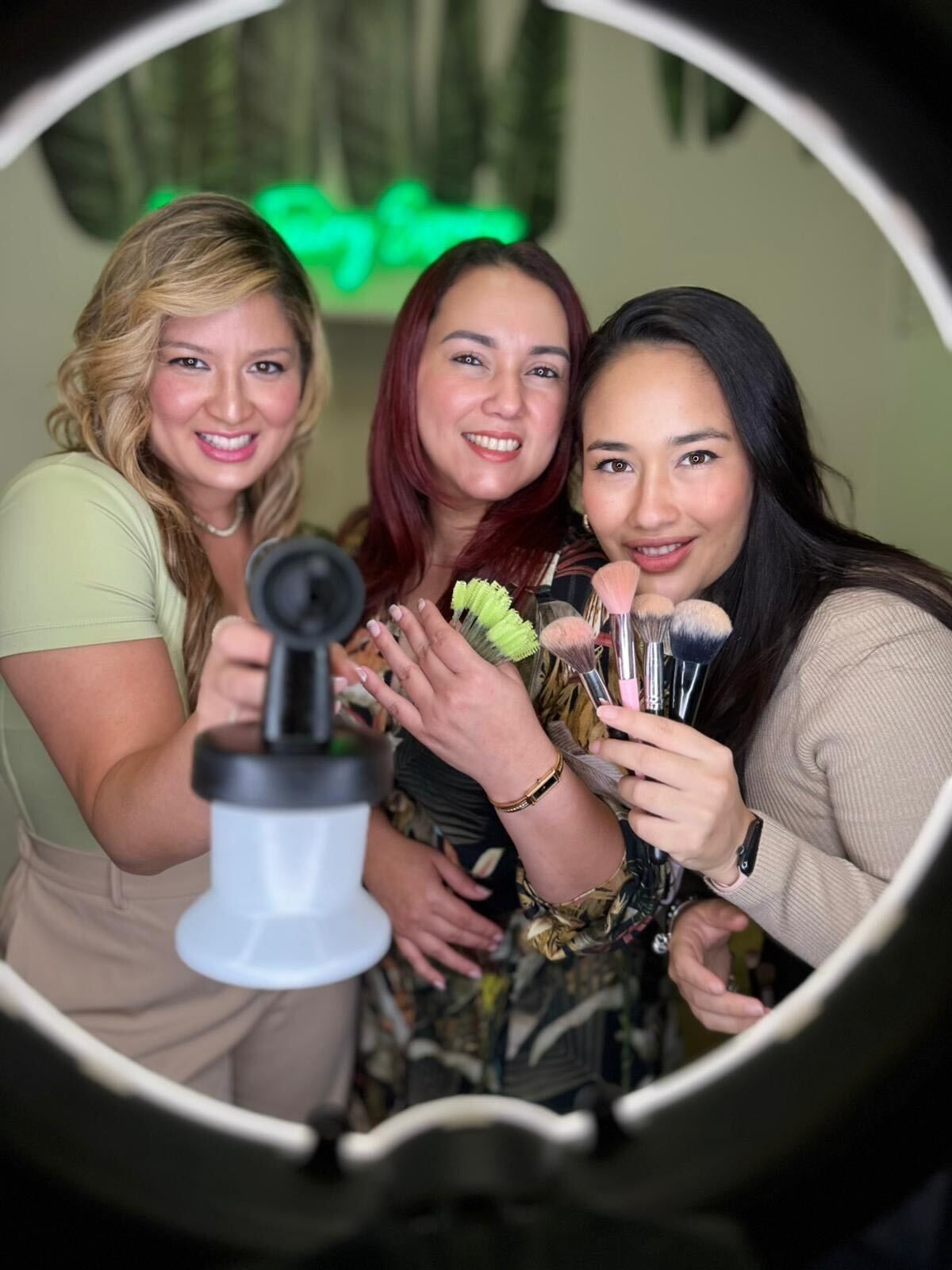 Three friends smiling with drinks in a ring light, posing at a party.
