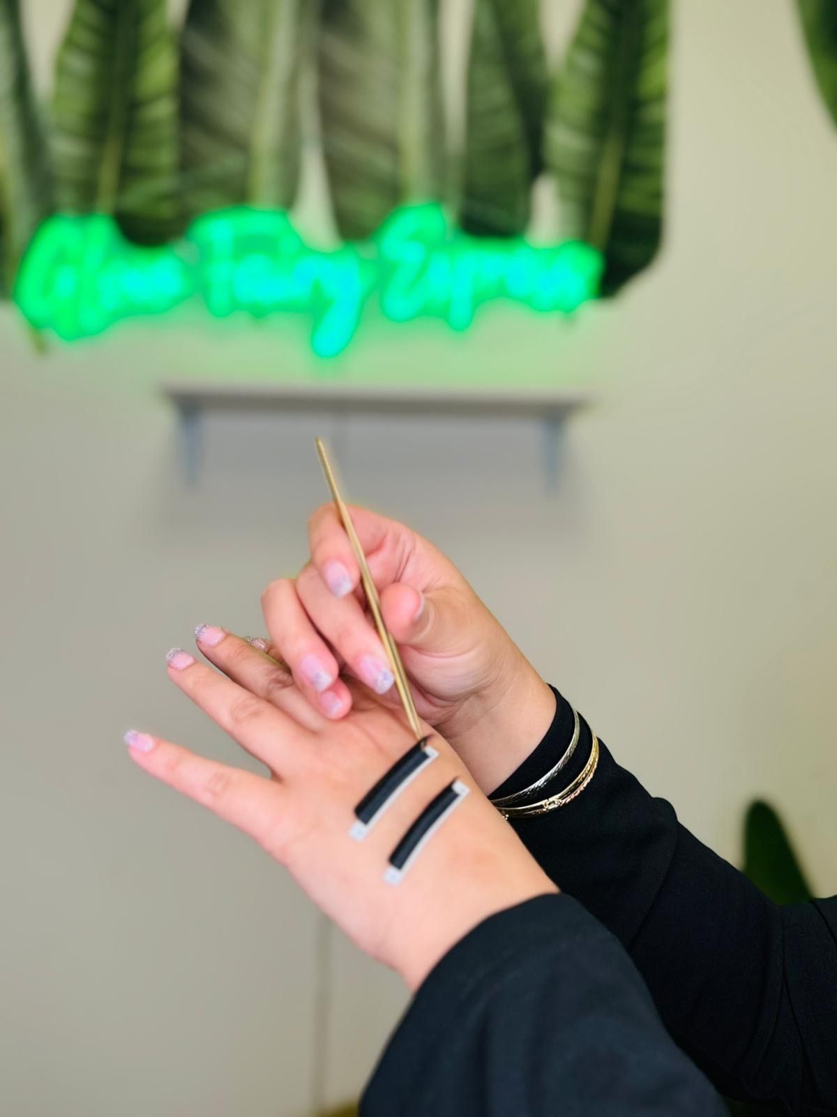 Hands showing nail art with two black stripes on the wrist, held against a blurred salon background.