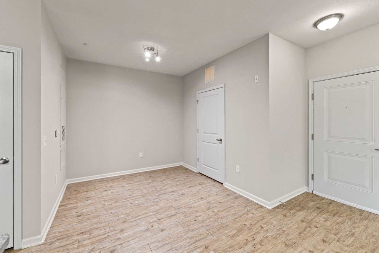 Empty apartment room with neutral walls, white doors, and wood-look flooring.