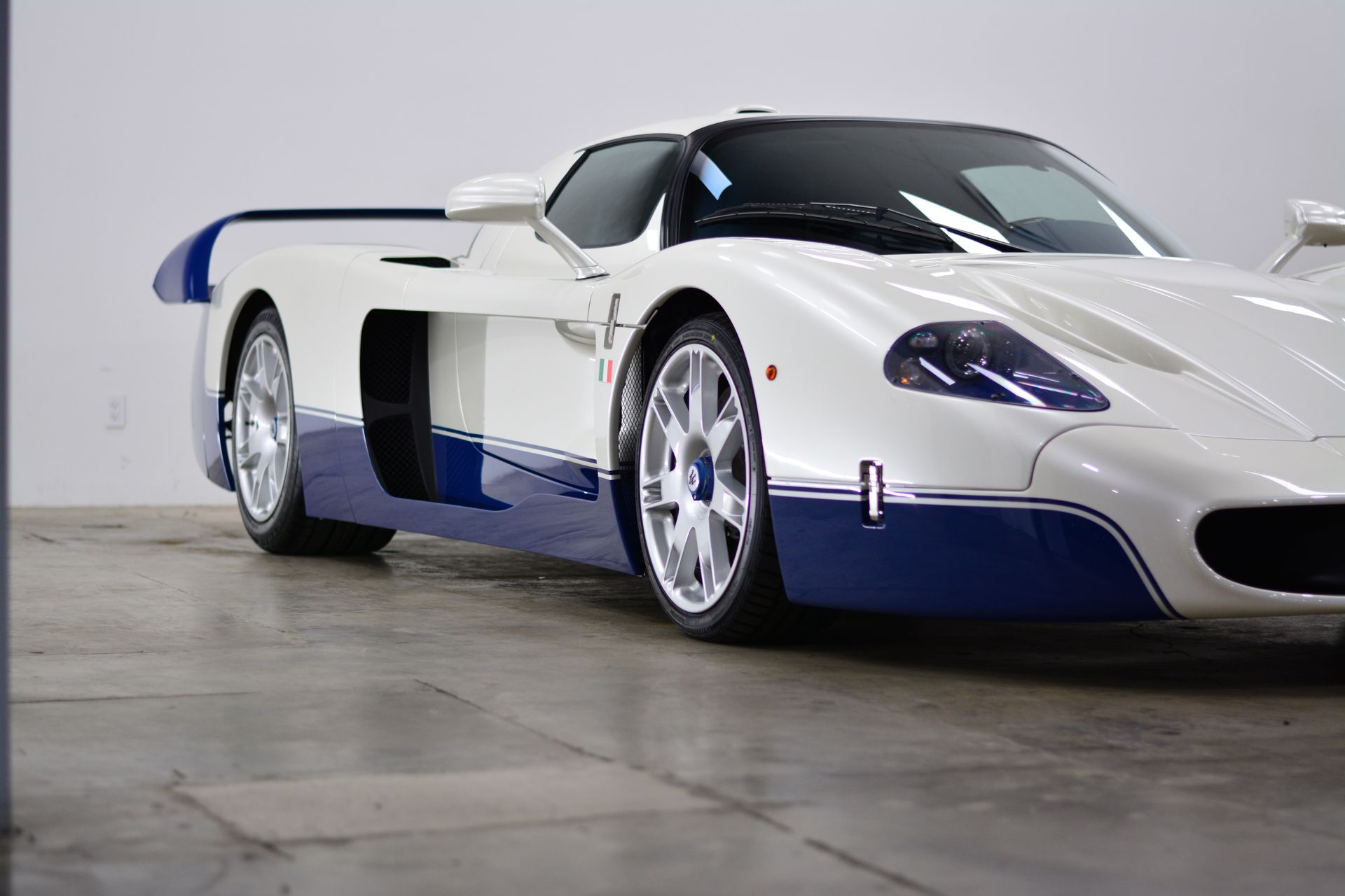 White and blue Maserati MC12 sports car on display in a showroom.
