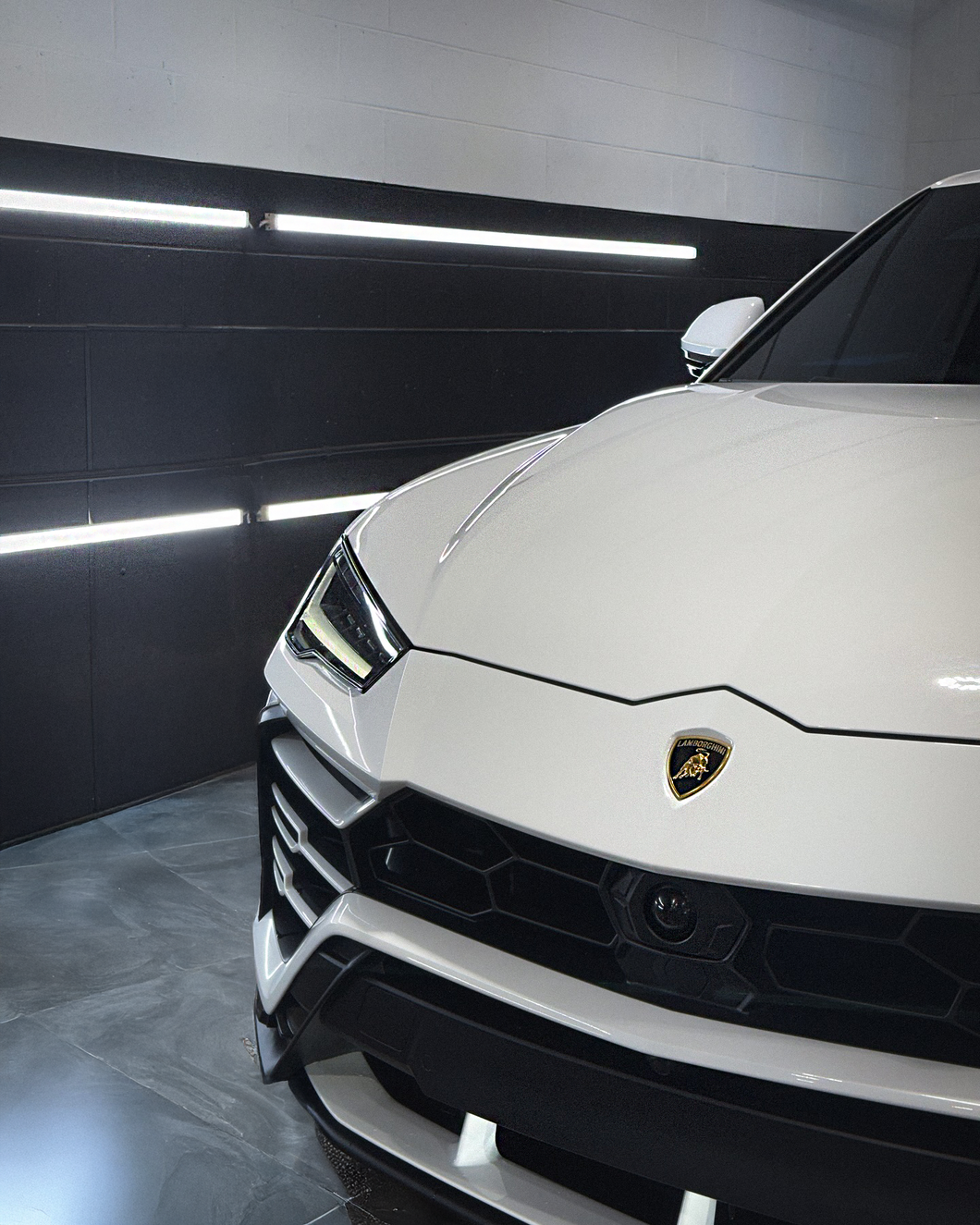 A white lamborghini urus is parked in a garage.