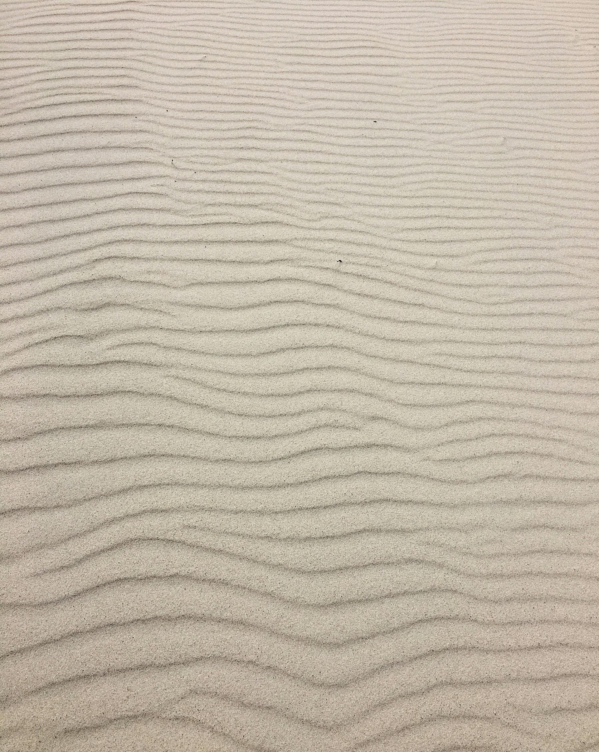 A close up of a sand dune with waves on it.