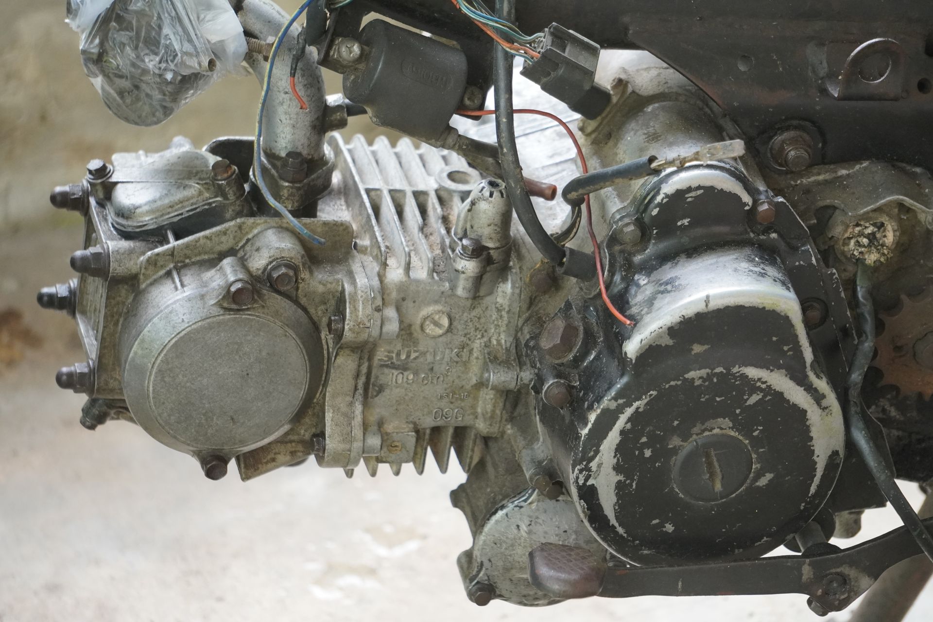 Dirty, used motorcycle engine with exposed cooling fins and a black side casing. Dirty, used motorcycle engine with exposed cooling fins and a black side casing.