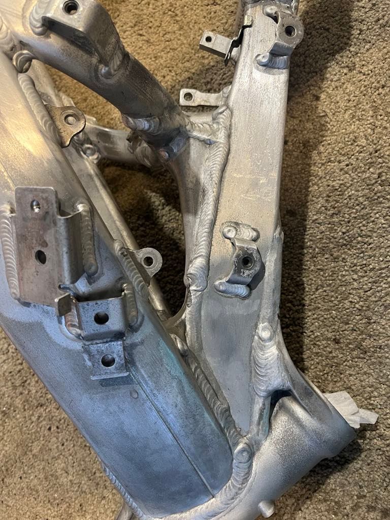 A close-up view of an unfinished aluminum motorcycle frame showing various welded mounting brackets and joints. A close-up view of an unfinished aluminum motorcycle frame showing various welded mounting brackets and joints.