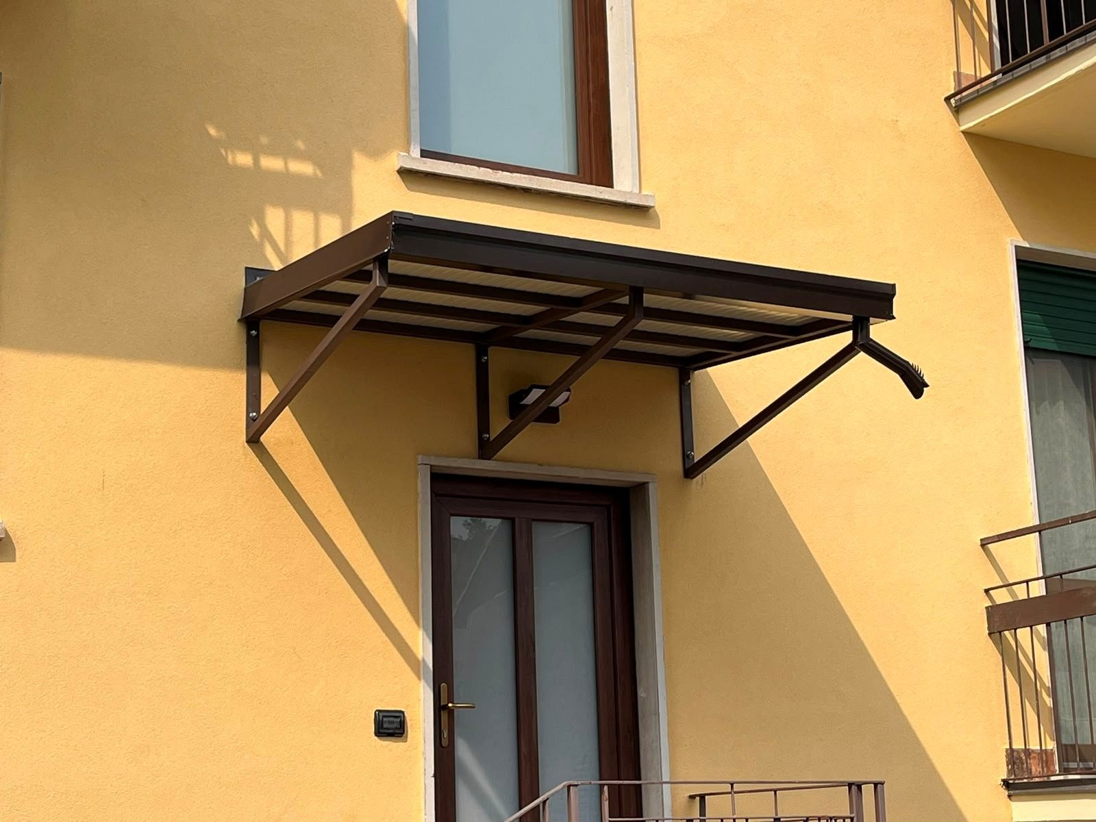Tenda da sole marrone sopra una piccola porta e una finestra sulla facciata gialla di un edificio.
