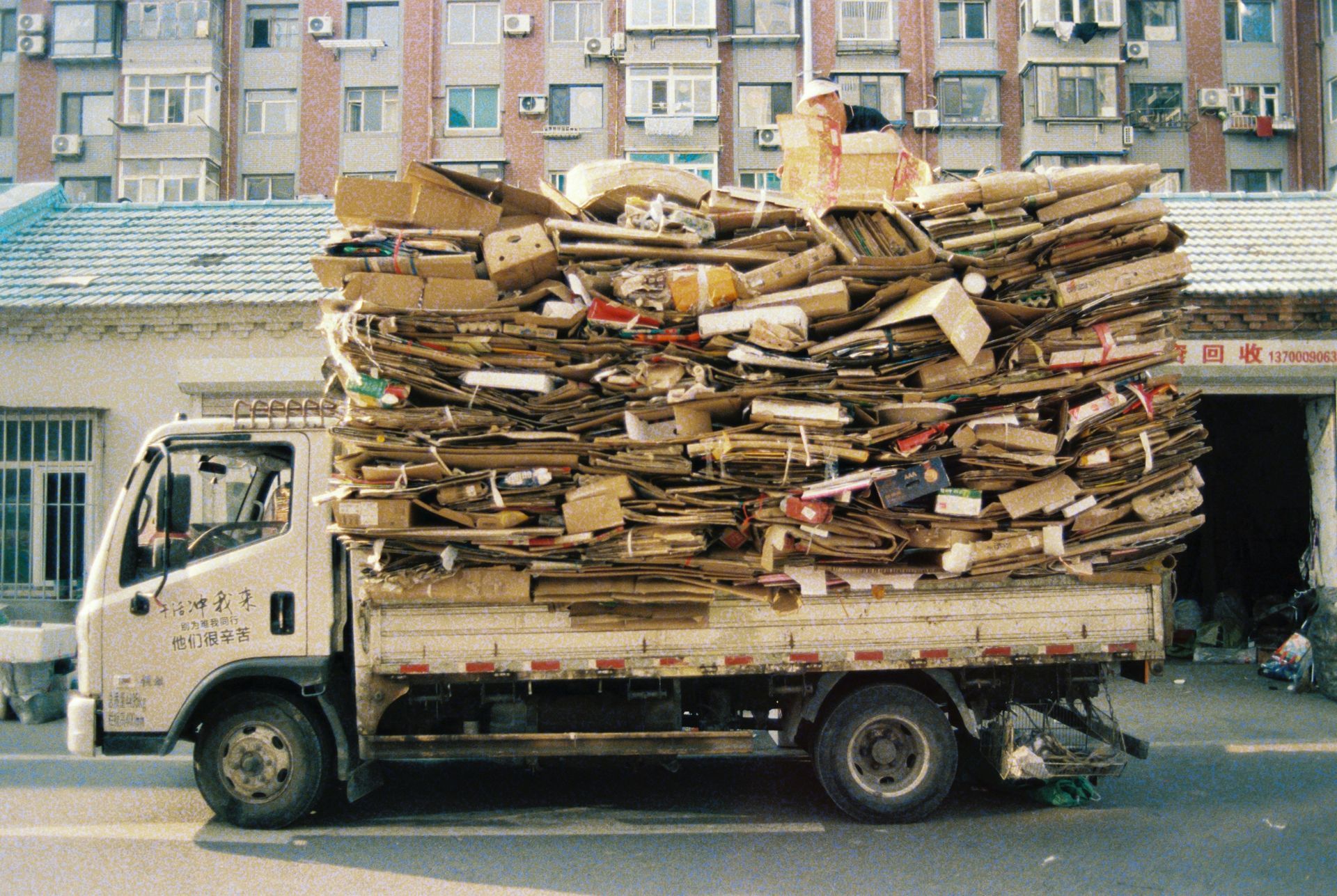 Worker in green and red uniform sorting debris into a bin from a rooftop or elevated platform
