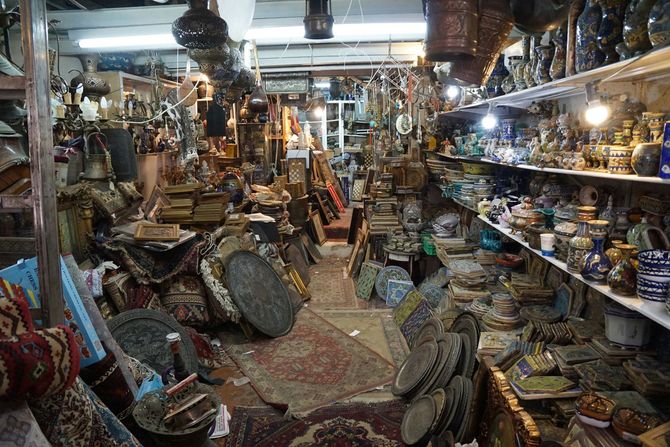 Cluttered antique shop packed with rugs, pottery, lamps, and ornate objects on shelves and floors