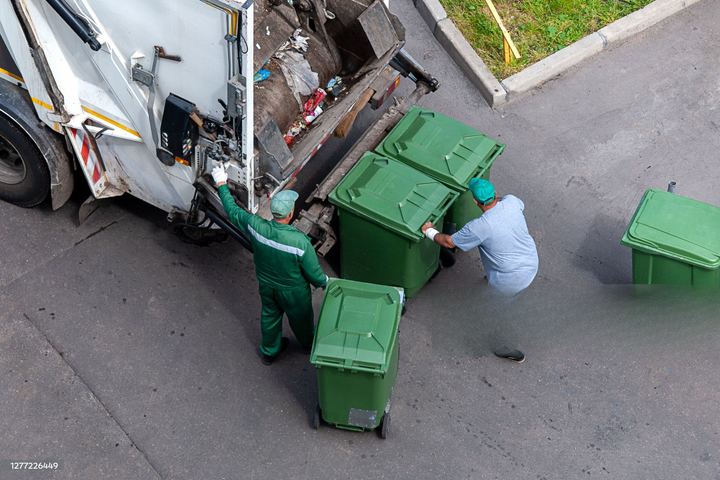 Garbage truck crew loading green bins onto a truck on a street