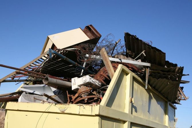 Collapsed metal and wood debris piled on a yellow dumpster under a blue sky