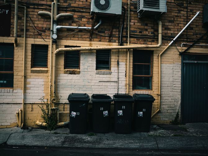 Garbage truck dumping trash into blue and yellow bins beside a brick wall outdoors
