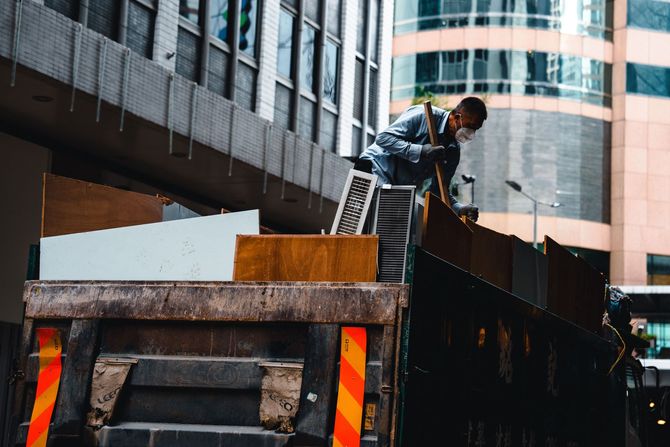 Worker loading debris into a dumpster beside a city building