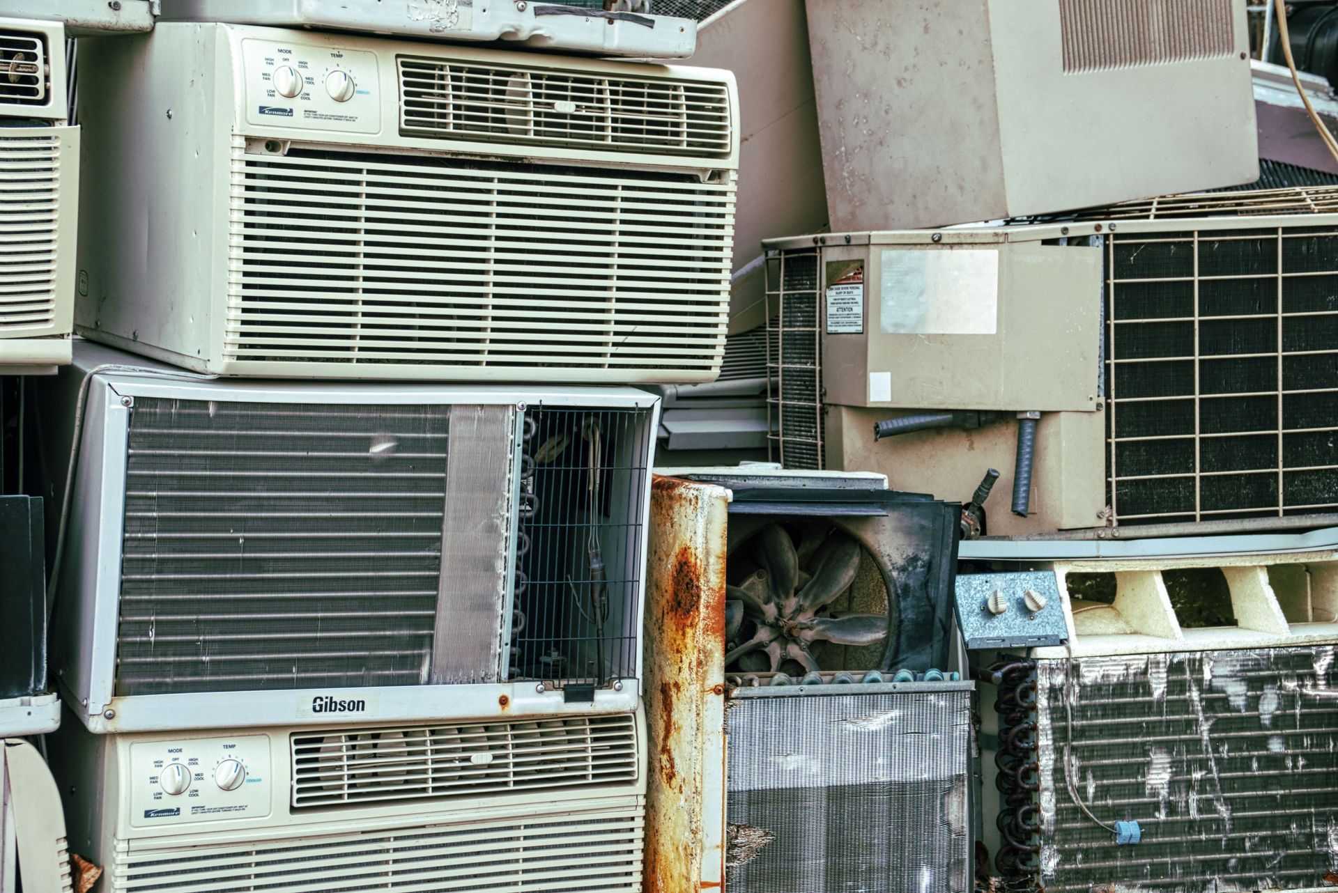 Stacked outdoor window air conditioners crowded against a wall, with rust and grime visible.