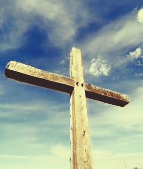 Wooden cross against a blue sky with clouds.