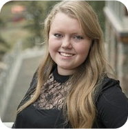 Woman with blonde hair smiling, wearing a black lace shirt, outdoors.