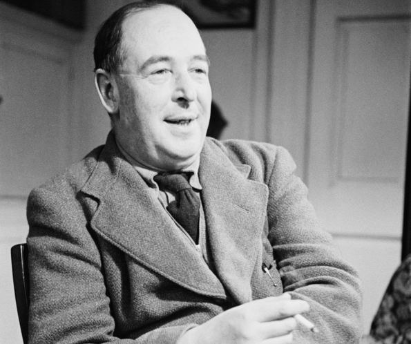 C.S. Lewis smiles, holding a cigarette. He sits indoors, wearing a suit jacket and tie.