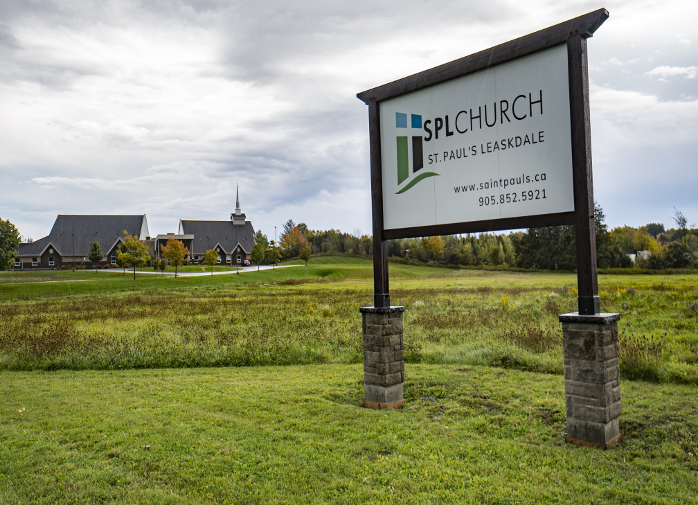 Church sign: SPL Church in St. Charles, with church building in background on a grassy field under cloudy sky.