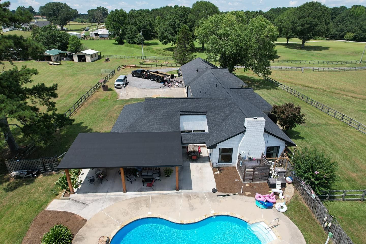 Aerial view of a house with a pool, patio, and dark roof on a grassy property.