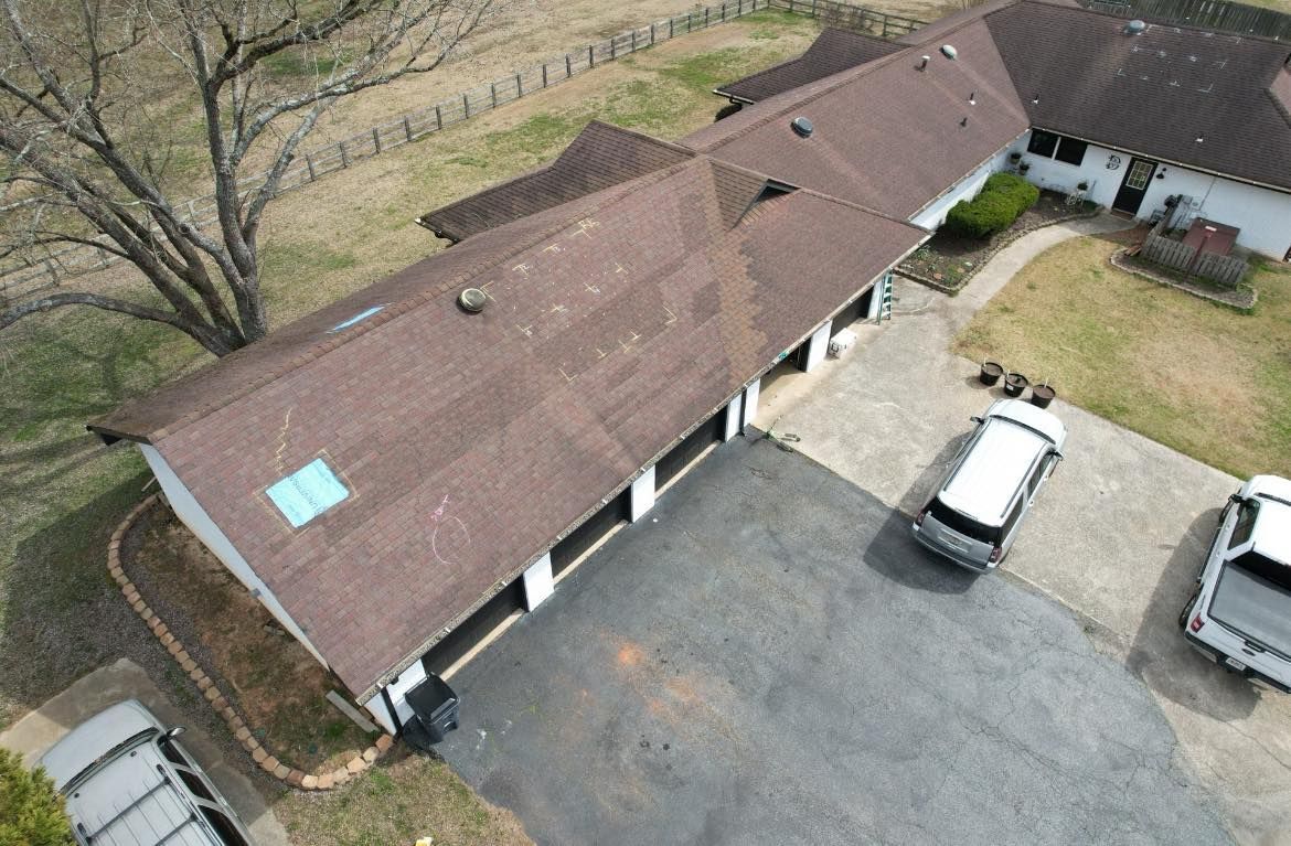 Aerial view of a brown-roofed house with a long driveway and three parked vehicles.