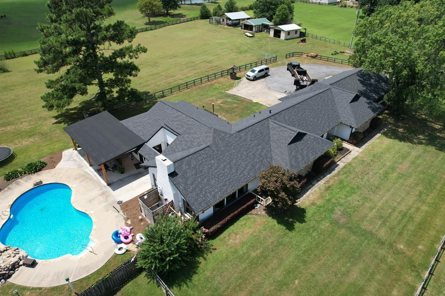Aerial view of a house with a dark gray roof, a pool, and surrounding green lawn.