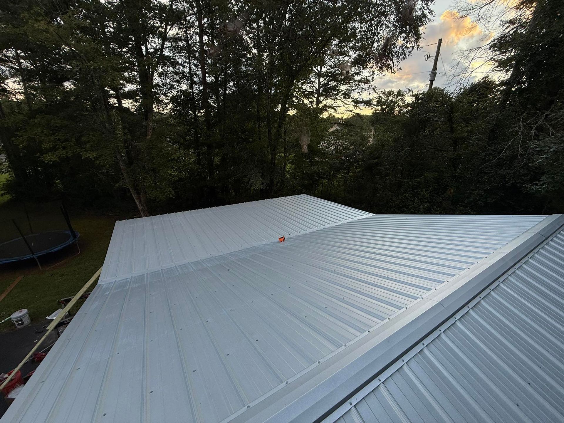 Metal roof with trees and twilight sky in background.