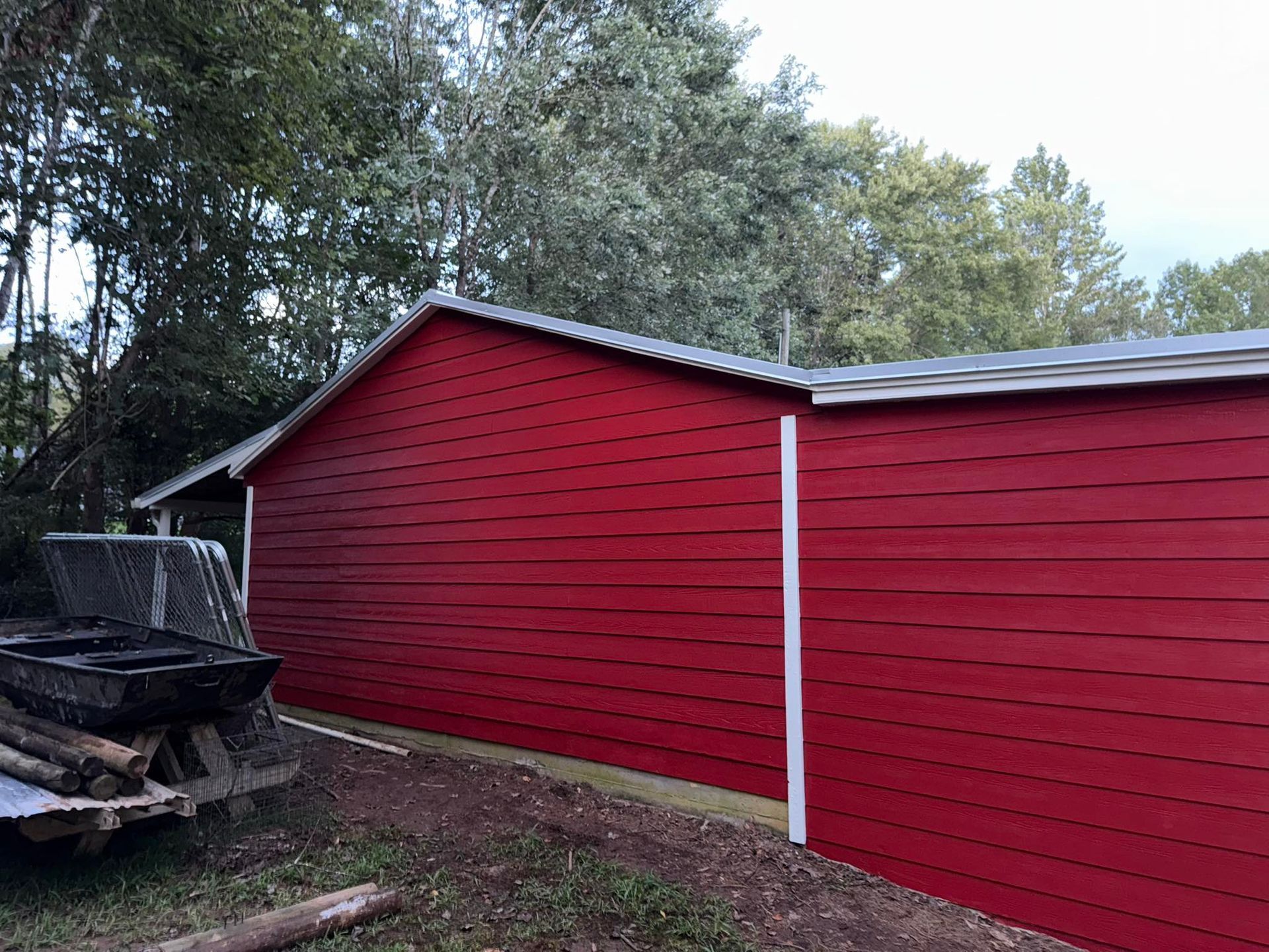 Red barn with white trim and metal roof, surrounded by trees.