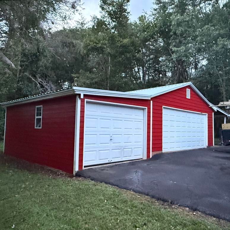 Red two-car garage with white doors, window, and trim. Asphalt driveway and trees in the background.