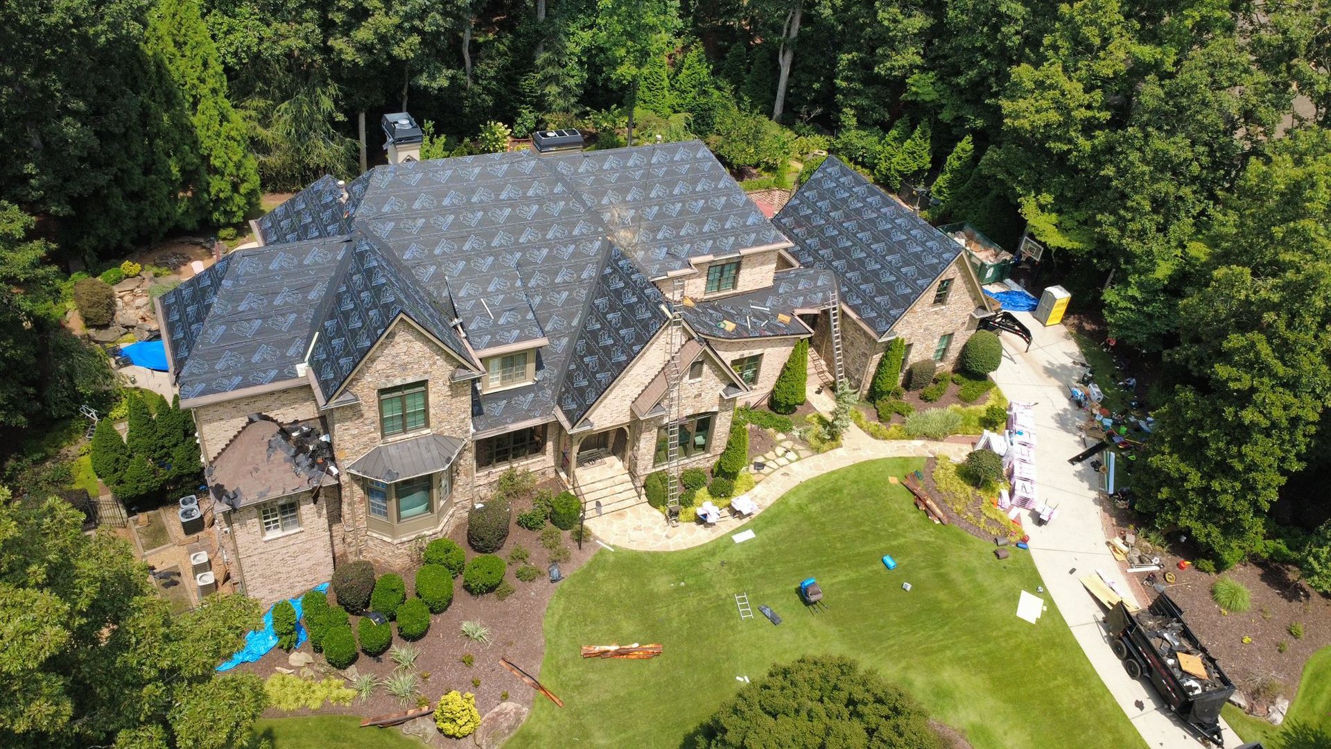 Aerial view of a large house with a newly shingled roof surrounded by trees and a green lawn.