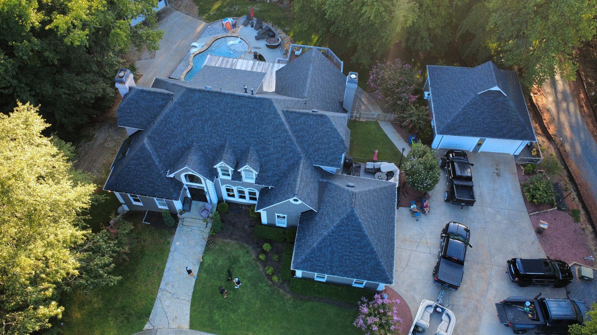 Aerial view of a gray house with dark roof, pool, driveway, and several black vehicles.