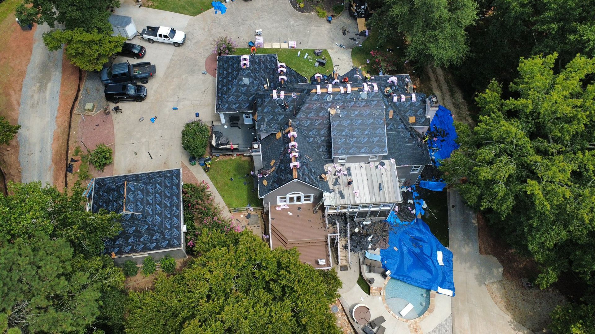 Aerial view of a house with roofing being replaced; blue tarps cover some sections.