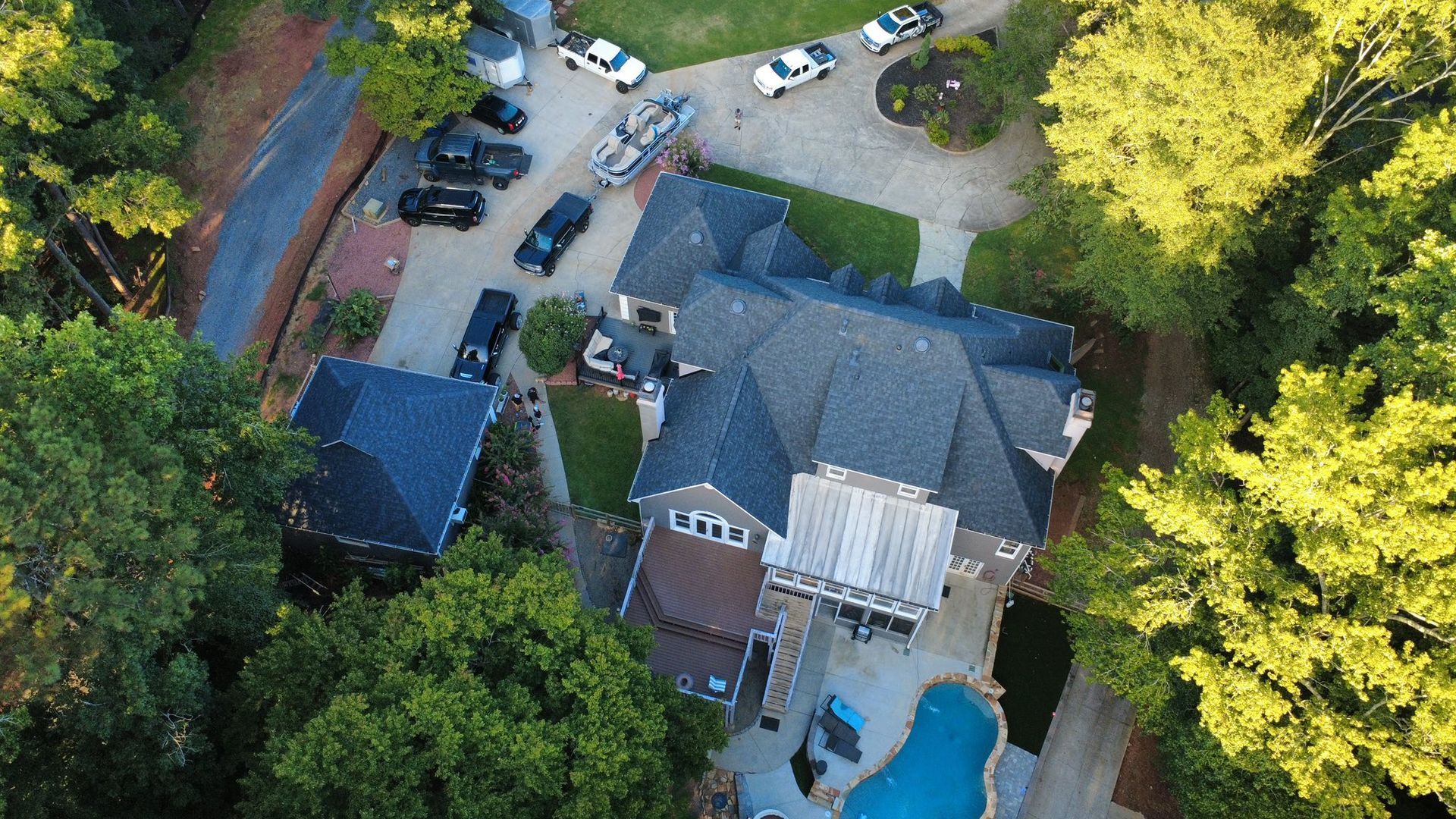 Aerial view of a large house with a pool, surrounded by trees and multiple police vehicles.