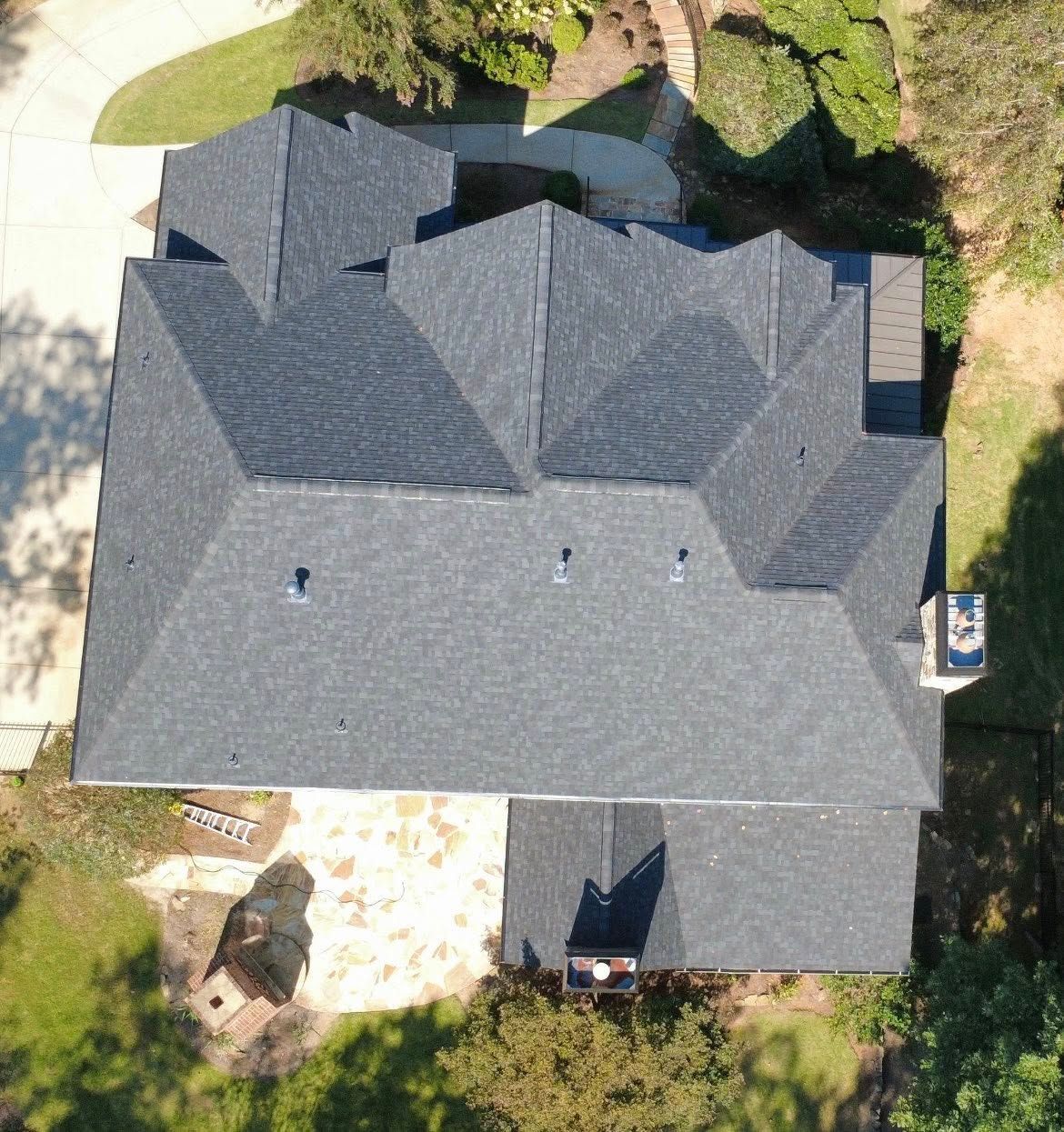 Aerial view of a dark gray shingle roof on a house, with a chimney and small skylights.