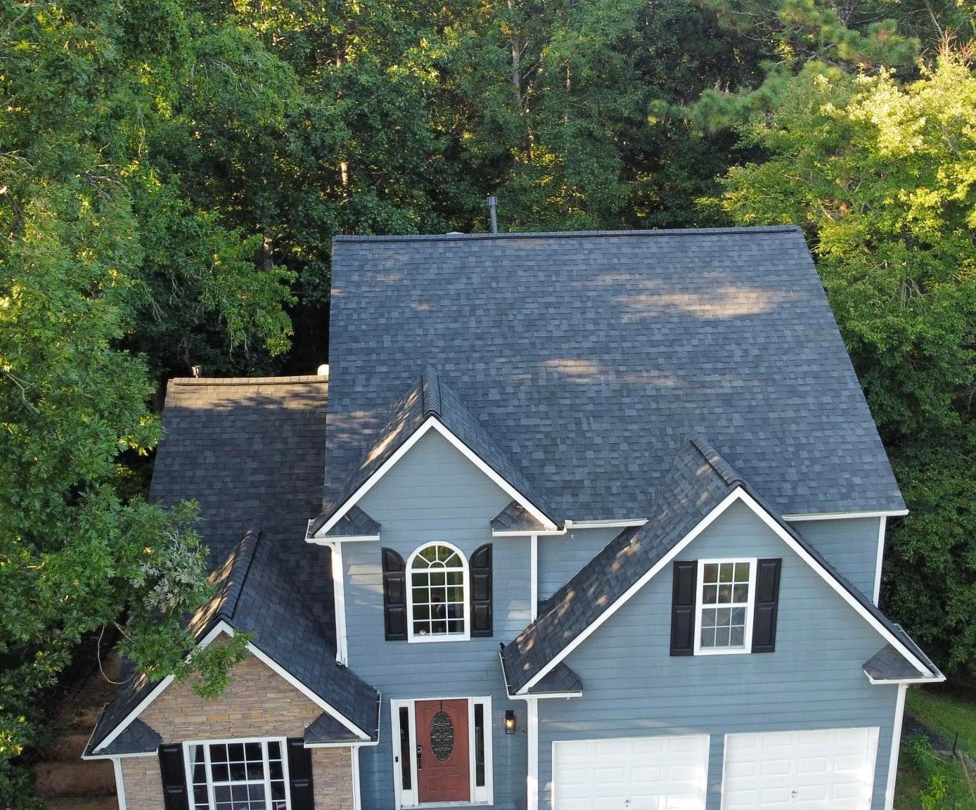 Blue house with dark roof and trim, surrounded by green trees.